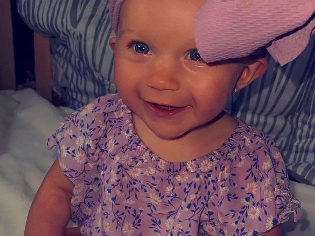 Nose, Smile, Cheek, Skin, Lip, Photograph, Eyebrow, Eyes, Facial Expression, Mouth, Purple, Cap, Baby & Toddler Clothing, Textile, Sleeve, Happy, Iris, Pink, Hat, Person, Headwear