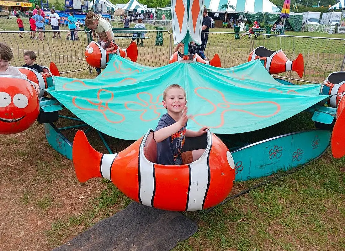 Smile, Leisure, Grass, Plant, Fun, Recreation, Flag, Tree, Event, Inflatable, Shade, Games, Carmine, Boats And Boating--equipment And Supplies, Sitting, Hat, Vacation, Personal Protective Equipment, Public Event, Person, Joy