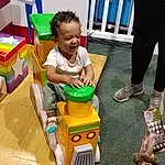 Shoe, Smile, Toddler, Toy, Leisure, Child, Baby Playing With Toys, Thigh, Baby, Recreation, Fun, Human Leg, Shorts, Sitting, Room, Toy Vehicle, Box, Play, Knee, Person