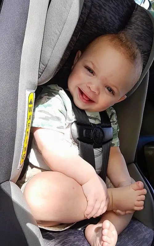 Smile, Skin, Leg, Comfort, Seat Belt, Gesture, Finger, Baby In Car Seat, Baby, Toddler, Thigh, Car Seat, Happy, Thumb, Car Seat Cover, Automotive Design, Baby & Toddler Clothing, Auto Part, Child, Steering Wheel, Person, Joy