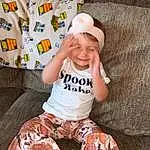 Head, Arm, Shorts, Smile, Baby & Toddler Clothing, Sleeve, Happy, T-shirt, Toddler, Thigh, Comfort, Pattern, Cap, Baseball Cap, Costume Hat, Linens, Child, Sitting, Couch, Fun, Person, Joy, Headwear