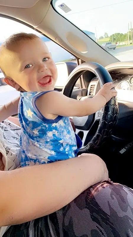 Skin, Smile, Vehicle, Car, Vroom Vroom, Steering Wheel, Baby & Toddler Clothing, Tartan, Automotive Design, Vehicle Door, Happy, Automotive Exterior, Toddler, Summer, Personal Luxury Car, Auto Part, Leisure, Thigh, Electric Blue, Human Leg, Person