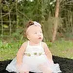 Skin, Plant, Eyes, Dress, Flash Photography, Baby & Toddler Clothing, Tree, Happy, People In Nature, Grass, Baby, Toddler, Headpiece, Jewellery, Headband, Peach, Bridal Accessory, Sitting, Hair Accessory, Fashion Accessory, Person