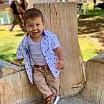 Smile, Shoe, Hairstyle, Leg, Wood, People In Nature, Happy, Leisure, Grass, Fun, Trunk, Sneakers, Toddler, Beauty, Tree, Recreation, T-shirt, Travel, Child, Sitting, Person, Joy