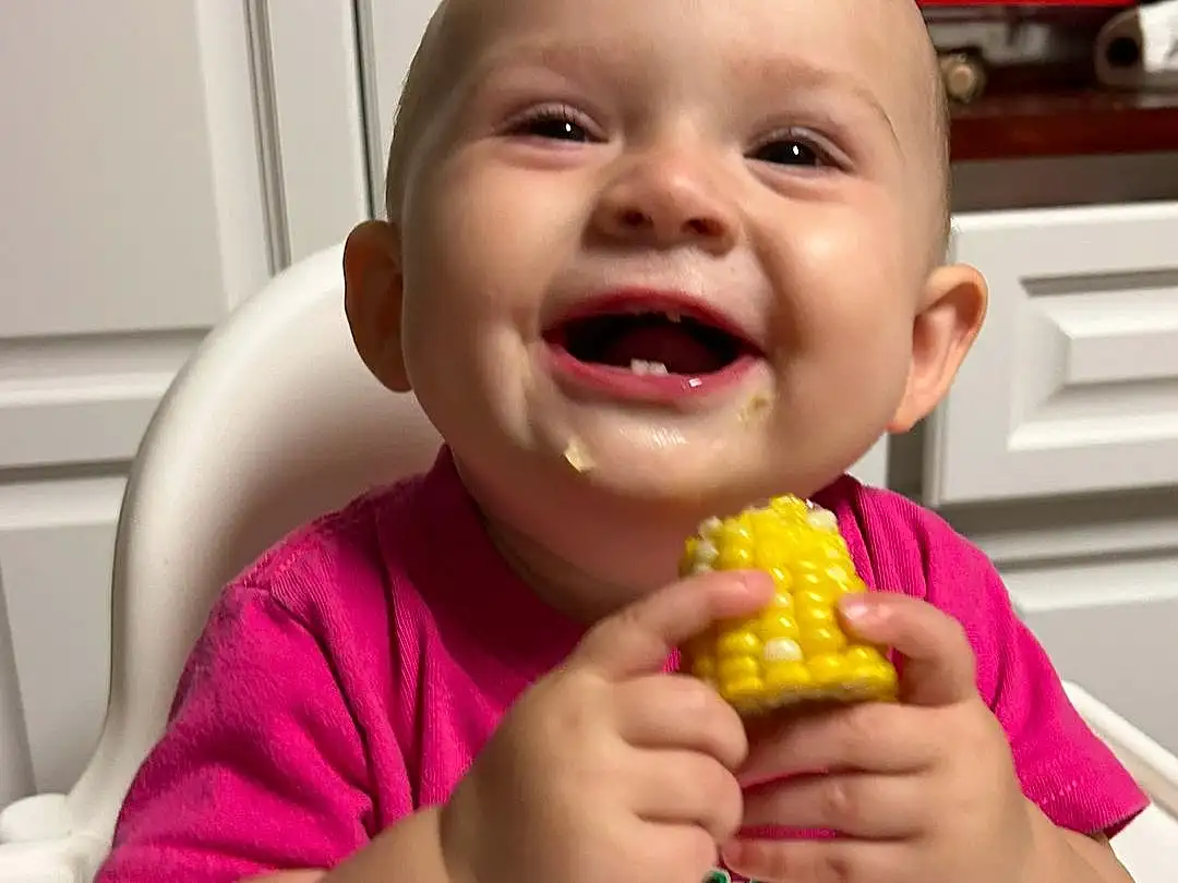Nose, Smile, Mouth, Food, Finger, Food Craving, Thumb, Happy, Fun, Toddler, Biting, Baby, Child, Sweet Corn, Sharing, Sweetness, Cuisine, Baby Laughing, Tableware, Play, Person, Joy
