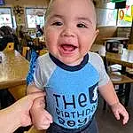 Smile, Cheek, Joint, Skin, Hand, Arm, Neck, Sleeve, Table, Gesture, Baby & Toddler Clothing, Finger, Happy, T-shirt, Thumb, Chair, Toddler, Baby, Child, Electric Blue, Person