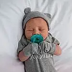 Clothing, Face, Nose, Skin, Head, Hand, Outerwear, Eyes, Arm, Mouth, Comfort, Sleeve, Baby, Baby & Toddler Clothing, Gesture, Flash Photography, Cap, Iris, Grey, Happy, Person, Headwear