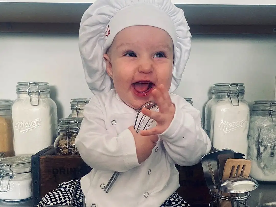 White, Tableware, Serveware, Drinkware, Kitchen, Toddler, Cooking, Happy, Cup, Kitchen Appliance, Baby & Toddler Clothing, Baby, Hat, Chef, Flash Photography, Smile, Sitting, Cook, Homemaker, Pattern, Person, Headwear