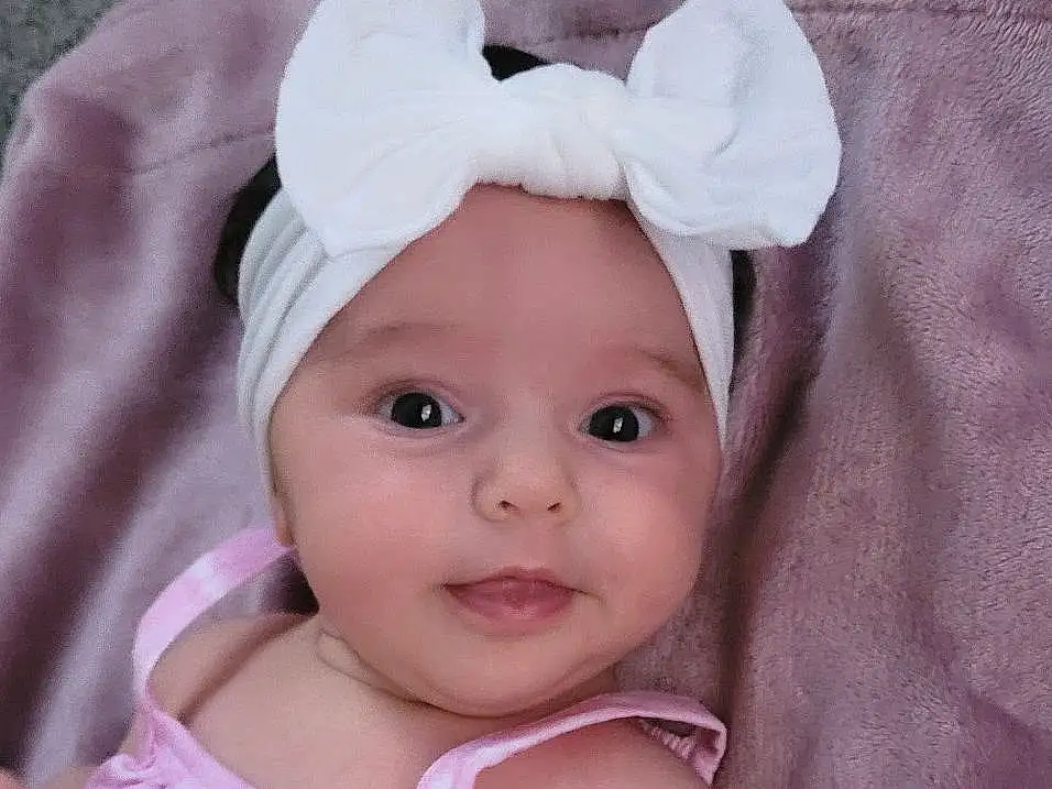 Nose, Cheek, Skin, Lip, Arm, Facial Expression, Human Body, Baby & Toddler Clothing, Sleeve, Iris, Comfort, Pink, Headgear, Toddler, Baby, Grass, Wood, Child, Sitting, Hair Accessory, Person, Headwear