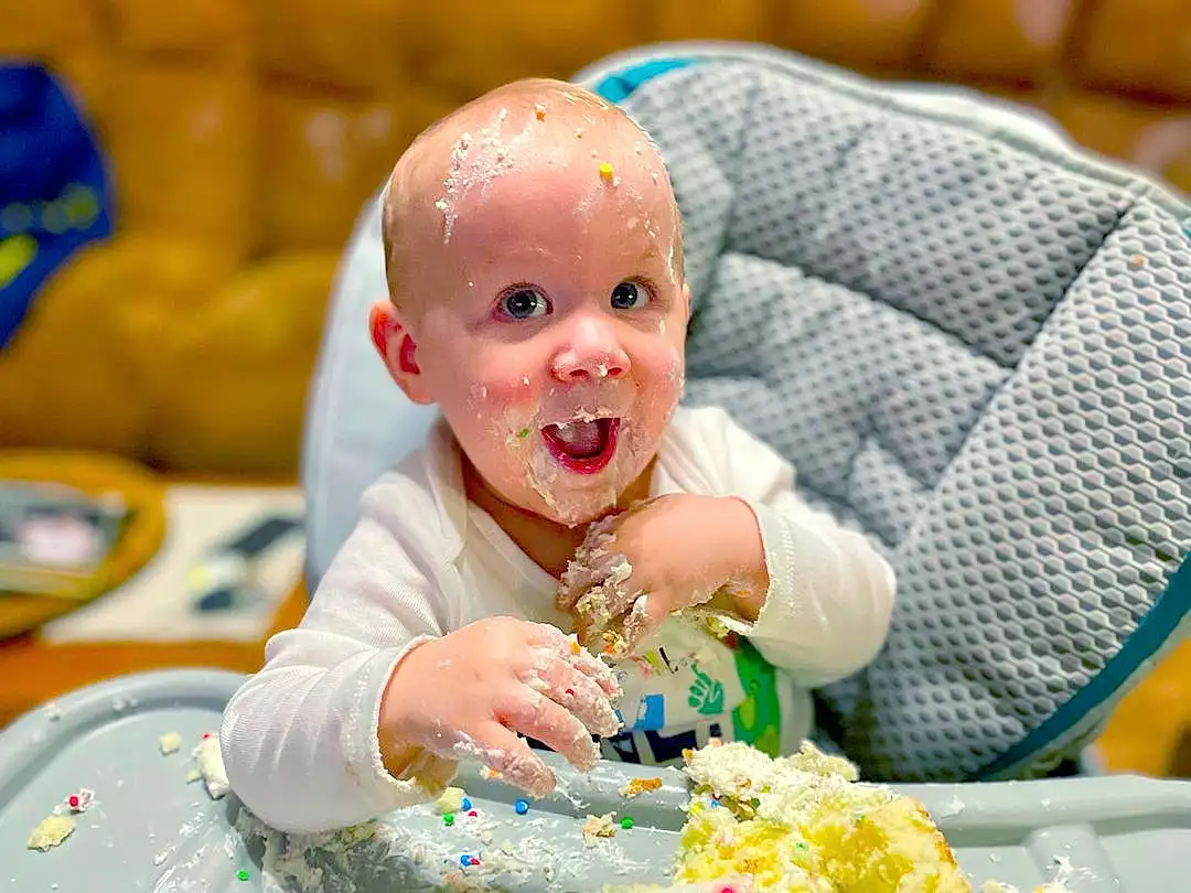 Smile, Food, Tableware, Table, Plate, Couch, Toddler, Baby, Happy, Recipe, Cuisine, Dish, Event, Child, Ingredient, Sweetness, Chair, Dessert, Sugar Cake, Comfort Food, Person, Surprise