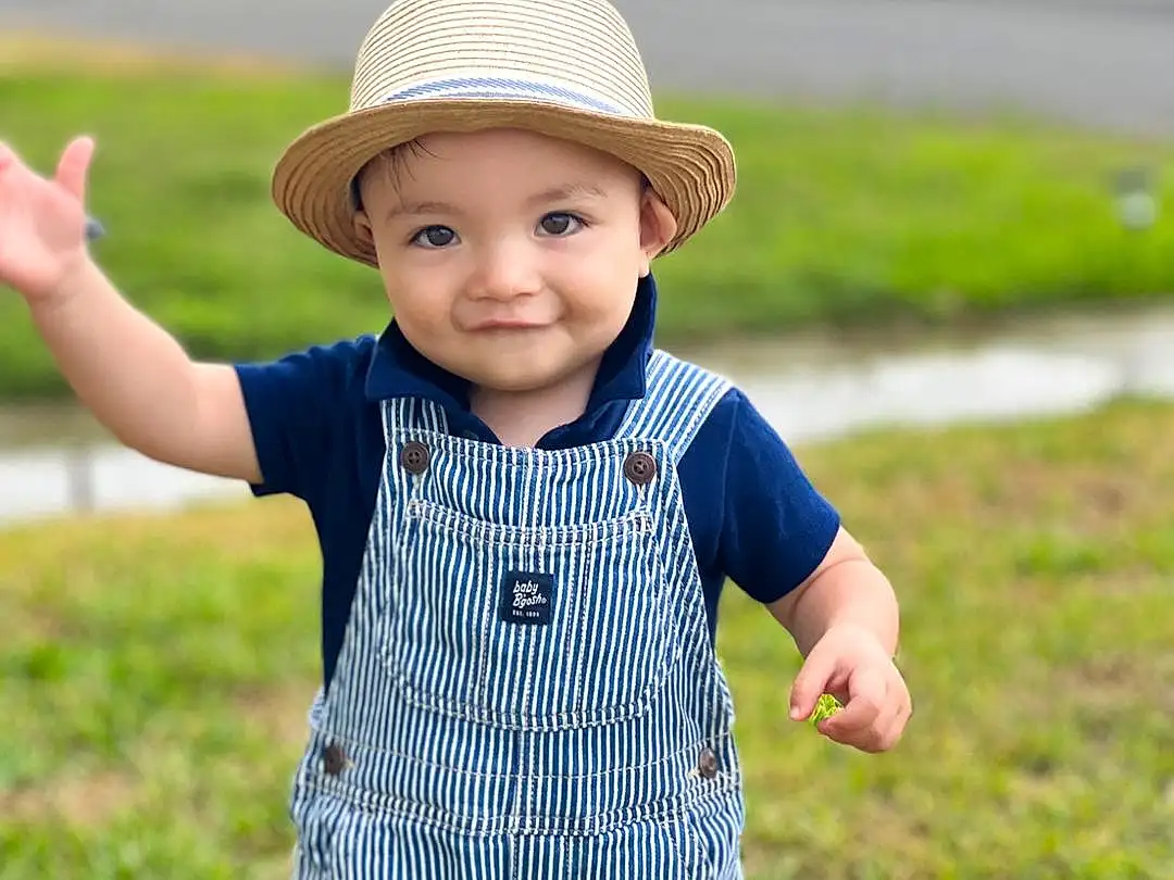 Smile, Outerwear, Facial Expression, Plant, Leaf, People In Nature, Hat, Baby & Toddler Clothing, Sleeve, Happy, Gesture, Headgear, Sun Hat, Cap, Baby, Grass, Toddler, Pattern, Fun, Person, Joy, Headwear