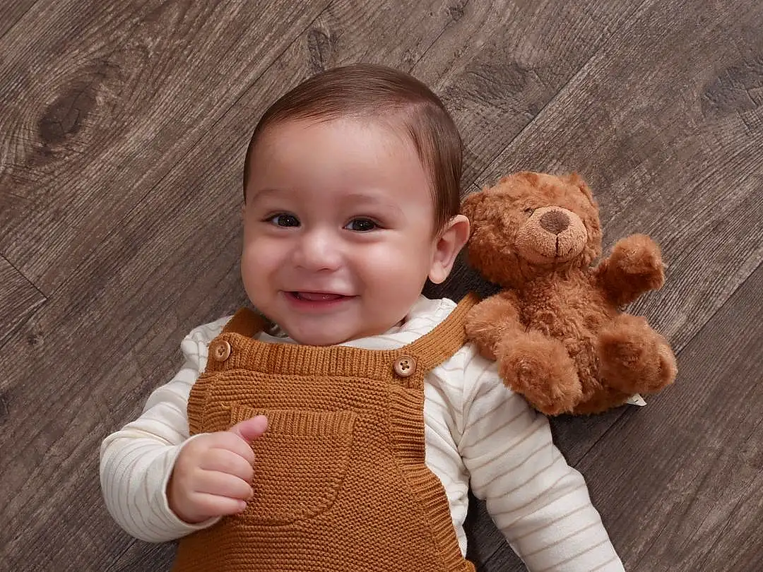Nose, Face, Brown, Cheek, Skin, Smile, Hand, Outerwear, Human Body, Sleeve, Gesture, Happy, Toy, Finger, Baby & Toddler Clothing, Wood, Thumb, Toddler, Baby, Stuffed Toy, Person, Joy