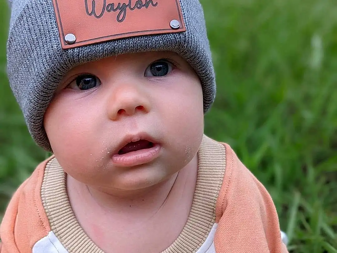 Cheek, Skin, Lip, Eyes, Cap, Sleeve, Baby, Happy, Baby & Toddler Clothing, Headgear, Grass, Toddler, Wool, Fashion Accessory, People In Nature, Pattern, Child, Hat, Knit Cap, Beanie, Person, Headwear