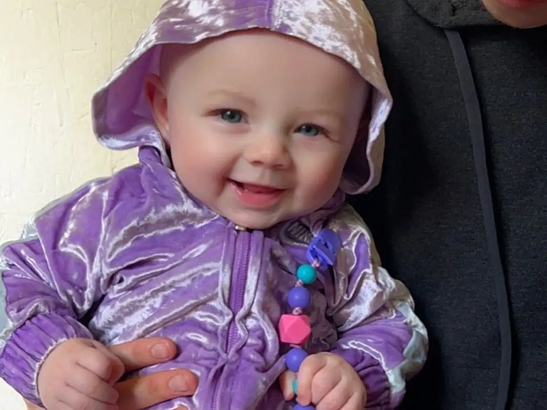 Clothing, Cheek, Skin, Outerwear, Smile, Purple, Sleeve, Cap, Baby & Toddler Clothing, Pink, Violet, Toddler, Happy, Baby, Child, Chair, Magenta, Electric Blue, Person, Joy, Headwear
