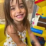 Smile, Skin, Hairstyle, Yellow, Happy, Fun, Toddler, Child, Beauty, Leisure, Recreation, Thigh, T-shirt, Sitting, Human Leg, Machine, Vroom Vroom, Toy, Chair, Person, Joy