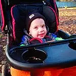 Smile, Baby Carriage, Vroom Vroom, Leisure, People In Nature, Comfort, Toddler, Plant, Child, Grass, Fun, Recreation, Travel, Baby Products, Tree, Electric Blue, Sitting, Auto Part, Personal Protective Equipment, Person, Joy, Headwear