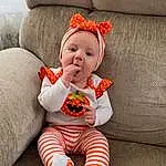 Cheek, Skin, Head, Outerwear, Eyes, Couch, Baby & Toddler Clothing, Baby, Sleeve, Orange, Comfort, Toddler, Smile, Sock, Child, Sitting, Pattern, Linens, Wood, Costume Hat, Person
